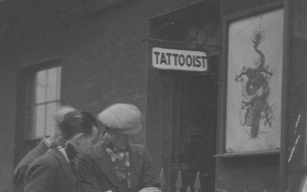 Two men getting tattoos outside a tattoo shop.