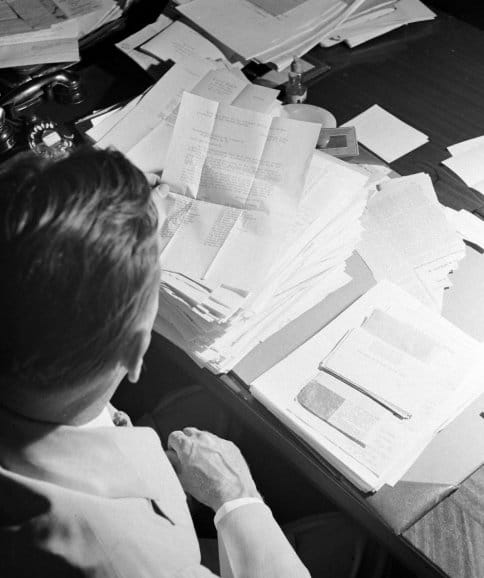 A Congressman sitting at a desk with a lot of papers.