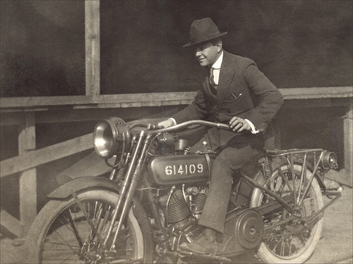 Vintage man riding motorcycle wearing suit fedora.