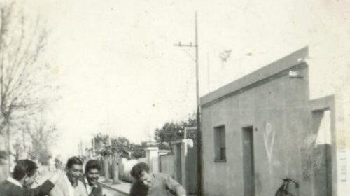 A group of men learning to ride a motorcycle on a street.