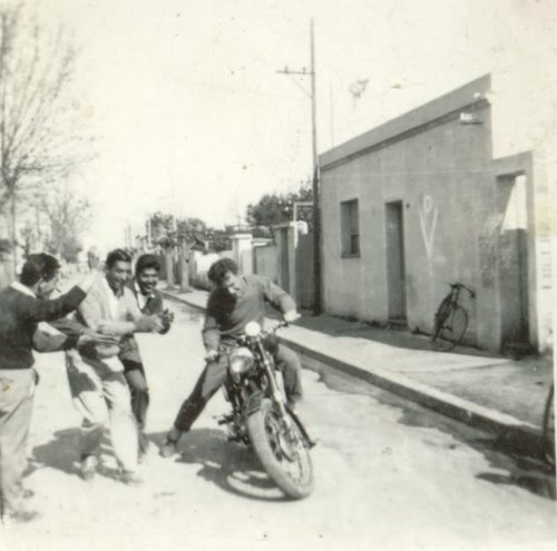 A group of men learning to ride a motorcycle on a street.