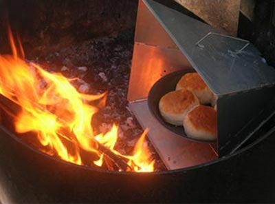 Reflector oven next to fire cooking biscuits.