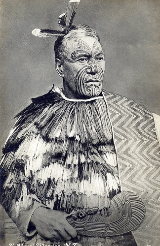 Native American man wearing war dress and tattoos on face.