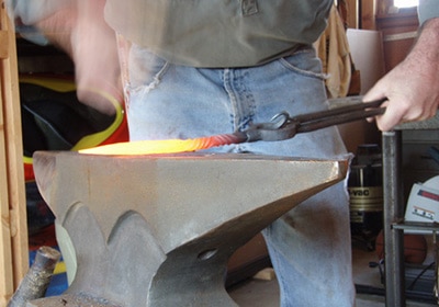 A man holding a hot iron and making cone on anvil edge.