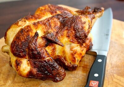 A delicious store-bought rotisserie chicken on a cutting board with a knife.