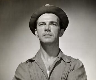 A black and white photo of a working man in a hat, showcasing his stylish dressing.
