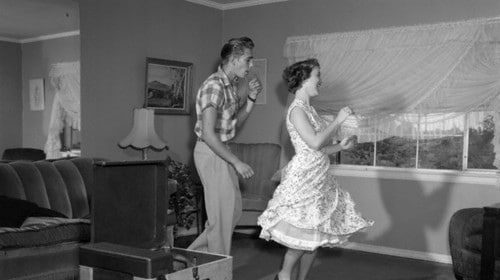 A man and woman joyfully dancing in a cozy living room with a record player, enjoying a romantic and affordable date night full of love.