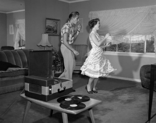 A man and woman joyfully dancing in a cozy living room with a record player, enjoying a romantic and affordable date night full of love.