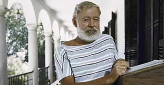A man with a beard and striped shirt is standing on a porch.