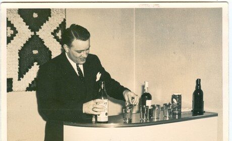 A stock image of a man in a suit pouring a bottle of wine at his home bar.