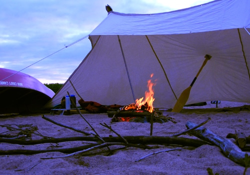 Lean to three sided tent camping shelter on beach with burning fire.