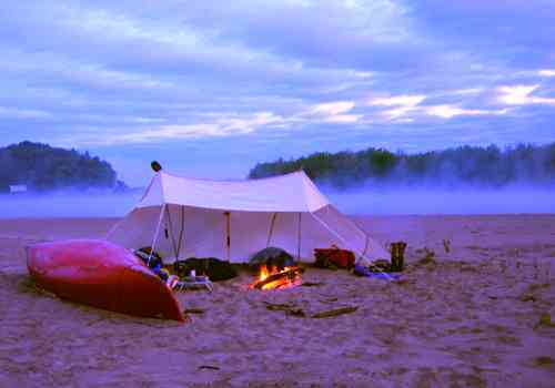 Lean to three sided tent camping shelter on beach with canoe.