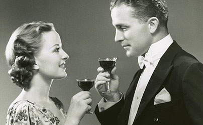 Vintage couple holding glasses of drink and looking at each other.