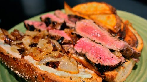 A sandwich with skirt steak and onions served on a green plate.