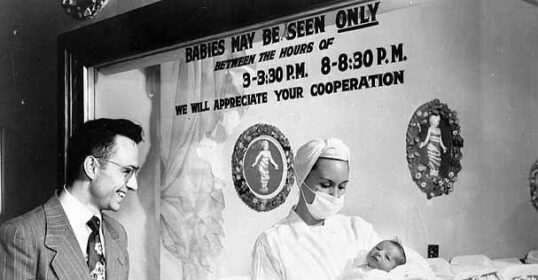 An old photo of a woman holding a baby in front of a mirror, capturing the precious moment of progeny.