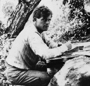 A man writing at a table in the woods.