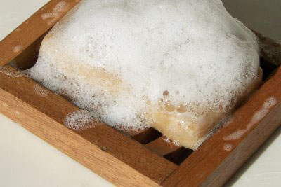 Soap covered in lather on wooden dish suds close up.