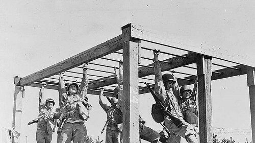 A group of fit GIs hanging from a wooden structure during World War II.