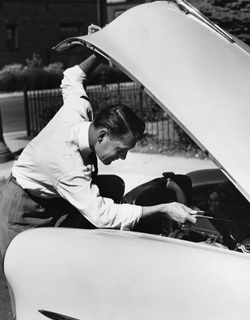 Vintage man lifting hood of car and working on engine.