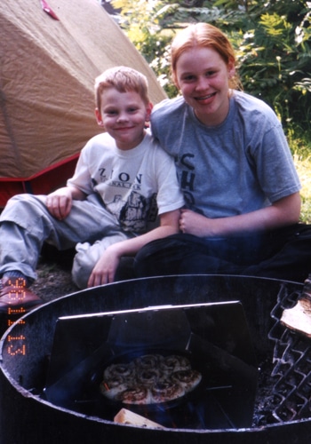 A mother and his kid cooking in a dutch oven.