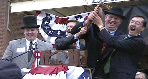 A men in campaign on stage holding ax and laughing.