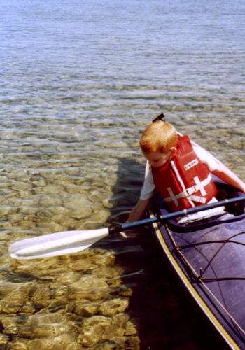 A kid wearing life jacket sit on a boat.