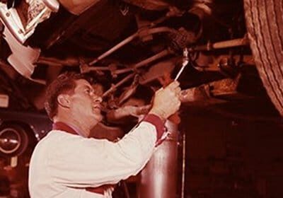 A mechanic performing auto troubleshooting on a leaking car in a garage.