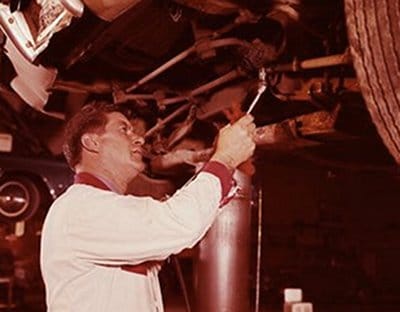 A mechanic performing auto troubleshooting on a leaking car in a garage.