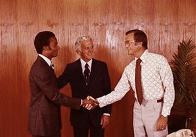 Three men shaking hands in front of a desk, sealing a successful selling deal with an effective pitch.