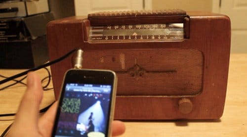 A person is holding an iPhone next to an old radio, showcasing the contrast between the modern mp3 player and the nostalgic old-time radio.