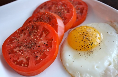 Fried egg with sliced tomatoes and pepper in the plate. 