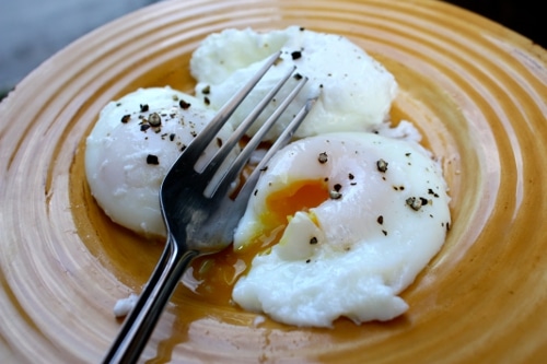 Poached eggs cracking in the plate with pepper and folk. 