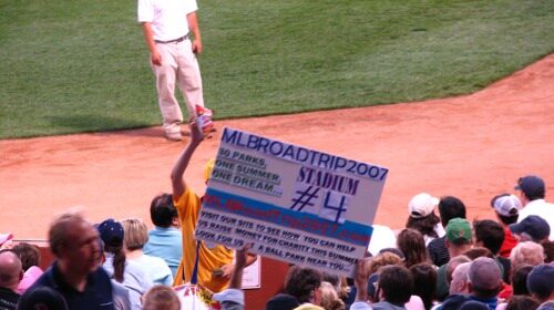 A man holding up a sign at a MLB game on his 30 Parks road trip.