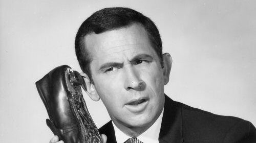 An old black and white photo of a man holding a shoe, showcasing his cool spy concealments.
