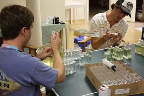Men filling moonshine cologne bottles in the basement of house.