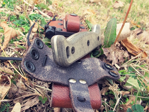 A knife with leather holster placed on the ground.