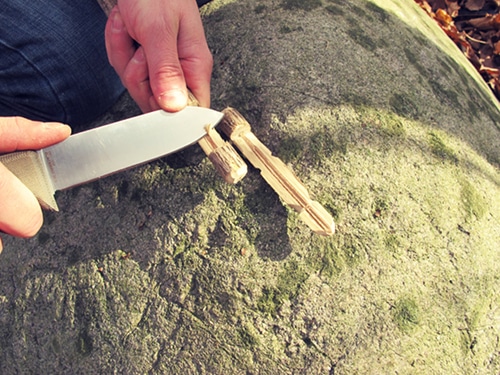 Large survival knife cutting small sticks branches.