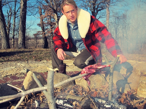 Ein Mann, der das Eichhörnchen auf dem Feuer brät.