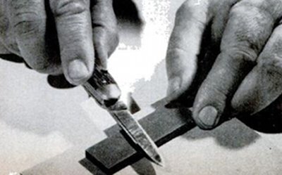 Vintage man sharpening pocket knife on stone.