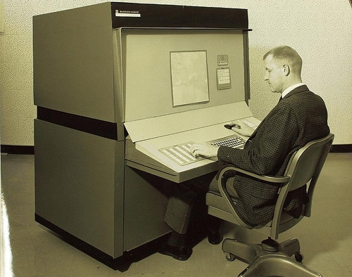 Vintage man working on a big computer machine in room.