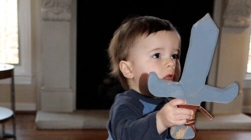 A kid wielding a wooden sword in front of a fireplace during a weekend DIY project.