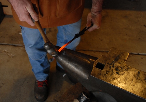 A man striking hammer on an iron.