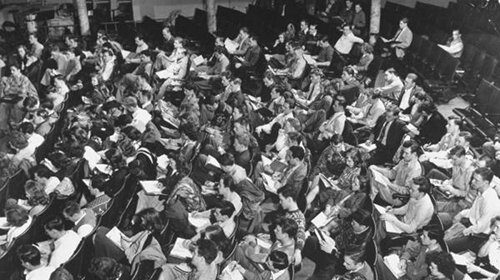 A large group of people sitting in chairs, engaged in note-taking strategies for academic success.