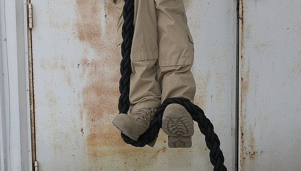 A man is hanging on a rope from a door as if he were a Navy SEAL training to climb.
