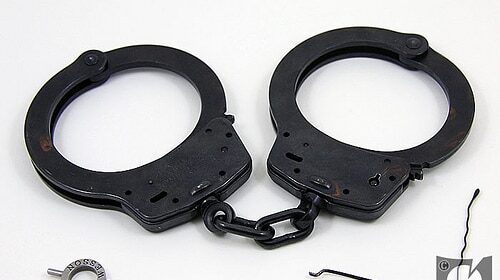 A pair of handcuffs lying on a white surface waiting for someone to pick them up.
