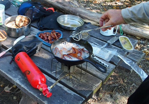 Man cooking bacon in portable camping stove at outdoors. 