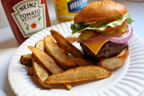 Bison burger with steak fries in paper plate with tomato ketchup. 