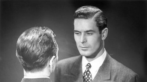 A man in a suit making eye contact with himself in the mirror to emphasize the importance of self-reflection and self-improvement.