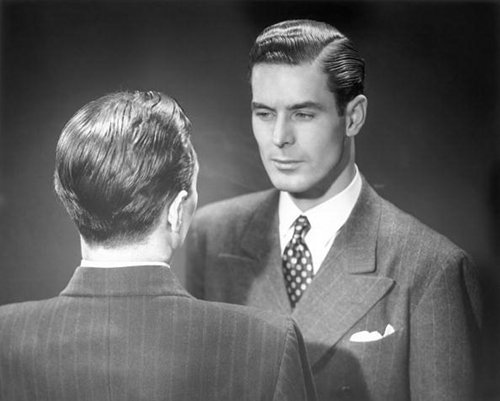 A man in a suit making eye contact with himself in the mirror to emphasize the importance of self-reflection and self-improvement.