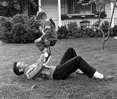 a dad horseplaying and wrestling with son on outside lawn 